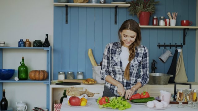 lachende vrouw die in de keuken allerlei groenten snijdt, zoals komkommer en paprika's
