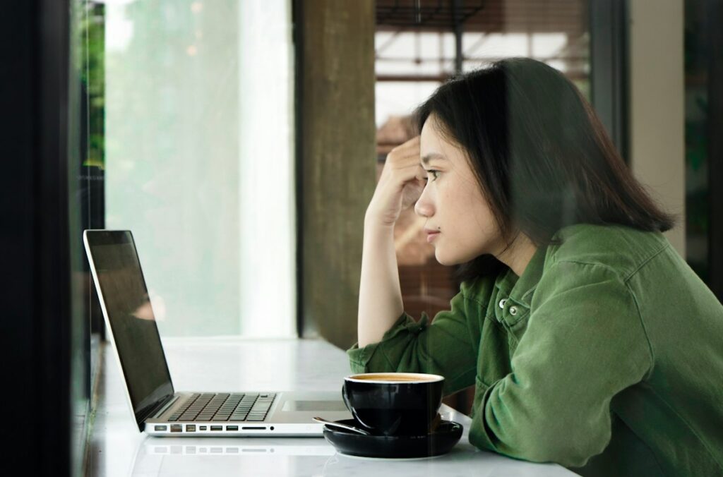 Vrouw kijkt piekerend naar haar laptop, met haar hoofd op haar hand
